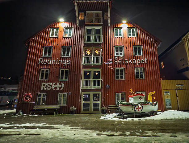 Tromso, Norway - December 21, 2025: Winter polar night. Red Cross on the official rescue on the sea services building and a small Christmas-decorated fake boat