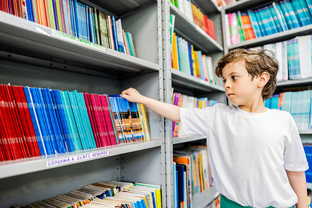 Schoolboy choosing books on the bookshelf at library at school