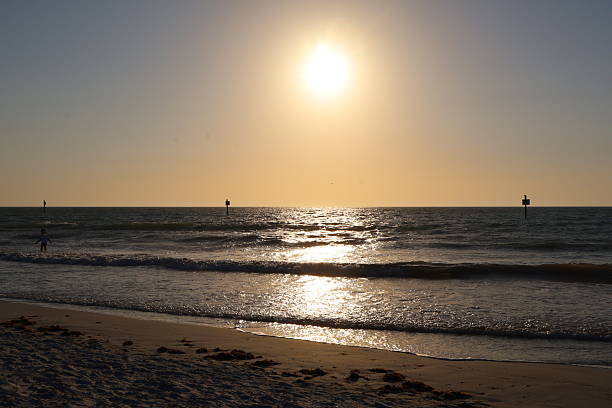 A tranquil beach scene shows gentle ocean waves rolling onto soft sandy shore.The yellow light coming from the sun on open horizon create a calming, airy atmosphere.The view reflects a quiet coastal moment on a sunny or late-day setting.