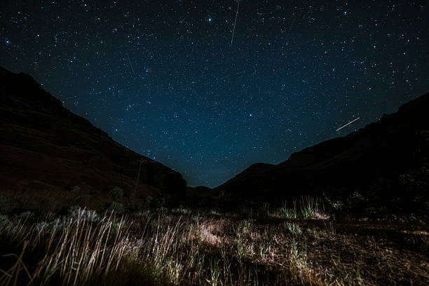 A clear night sky filled with stars stretches above a rugged high-desert canyon landscape in Central Oregon.