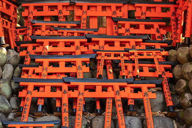 Kyoto, Japan - December 07, 2025: A close-up view of countless vibrant orange mini torii gates, donated and stacked on a rocky embankment at Fushimi Inari-taisha Shrine, showcasing a unique
