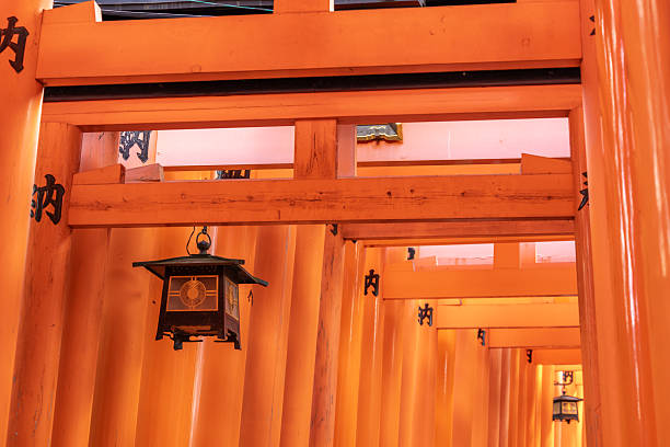Kyoto, Japan - December 07, 2025: Vibrant orange torii gates create an iconic tunnel leading through Fushimi Inari Taisha shrine, adorned with traditional Japanese lanterns. A spiritual journey