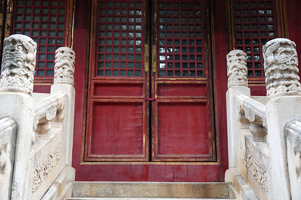 Traditional Chinese architecture features ornate red wooden doors with stone carvings. This image showcases classic architectural details, including lattice windows and decorative stone columns.