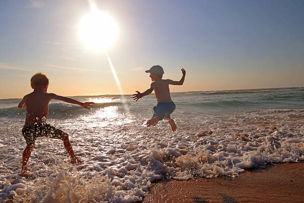 Two boys jump in ocean waves at sunset, Bordeaux