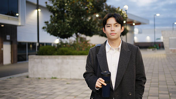 Young asian man walking with reusable coffee cup on an urban street at dusk