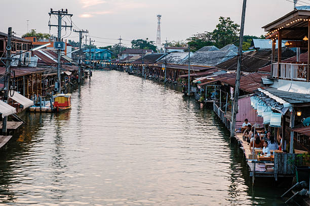 Amphawa Floating Market, Thailand 5 December 2025. Experience a vibrant scene with wooden stalls by the water, while locals and tourists enjoy delicious street food as the sun sets over the market.