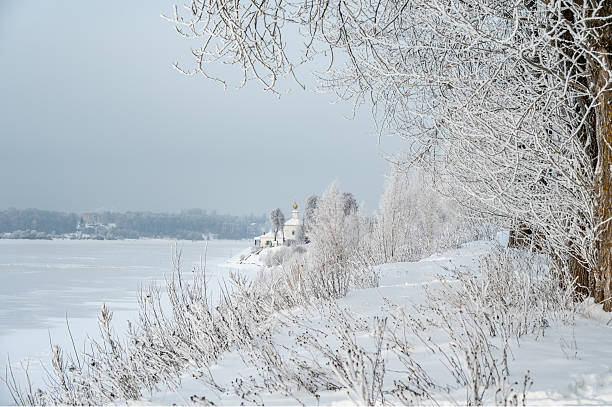 Small rural ancient Orthodox Temple on river bank covered with snow.