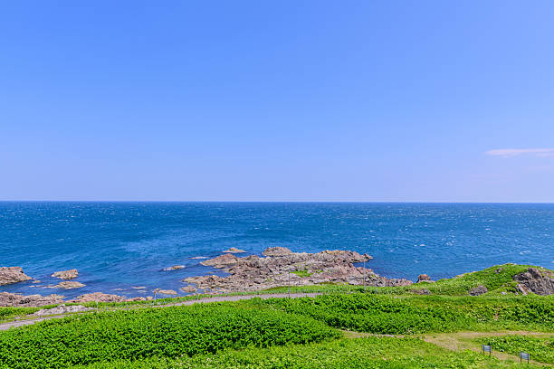 A tranquil summer view of Cape Kamui in Kitami, Hokkaido, Japan. The scene is filled with deep blue skies and vast ocean under brilliant sunlight, capturing the peaceful atmosphere of northern Japan.