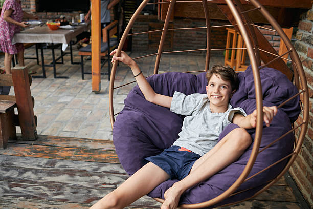 Young boy smiling and relaxing in a hanging egg chair on a backyard patio