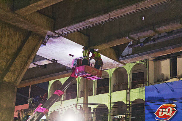 Skalmierzyce, Greater Poland Voivodeship, Poland - september 26, 2025 A worker wearing high-visibility clothing conducts maintenance on the bridge support while standing in an aerial lift basket beneath the road overpass structure.