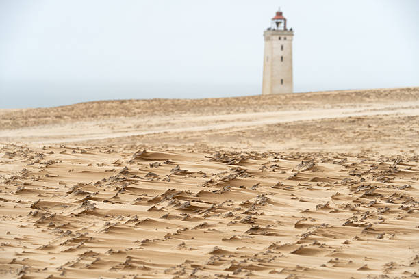 Textured wind-crusted sand with Rubjerg Knude lighthouse in the background.