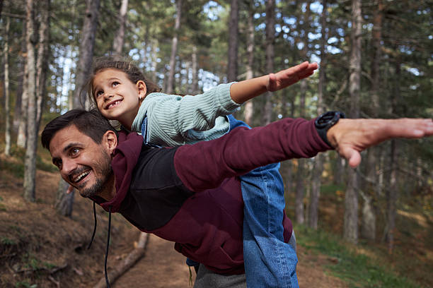 Father and daughter having fun playing together on a piggyback ride in the forest