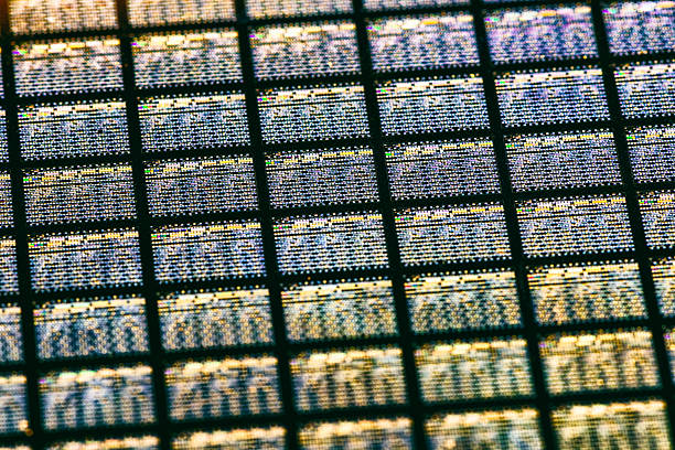 A detailed macro view of a semiconductor or microchip surface, revealing a precise grid structure illuminated by shimmering, multicolored reflections. The image emphasizes advanced technology, data processing, and digital complexity, making it suitable for concepts related to computing, electronics, innovation, artificial intelligence, and modern industrial design.