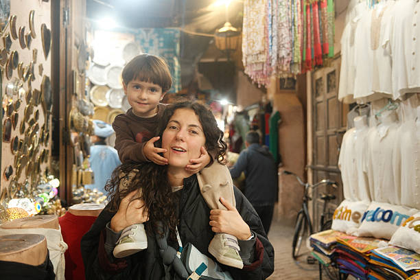 Mother and young son enjoying a piggyback ride, exploring a vibrant market alleyway in Marrakech, Morocco