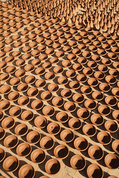Array of traditional artisanal clay pottery components air drying under the sun, creating repetitive patterns and shadows