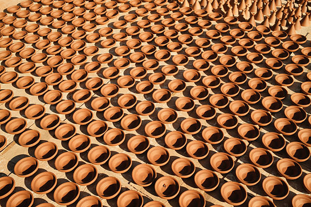 Terracotta pots and bowls drying in perfect rows under strong sunlight, creating shadows. Handmade clay pottery craft