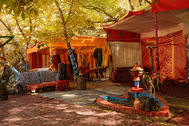 Moroccan traditional tent displaying colorful textiles, carpets, and robes under autumn trees, featuring an ornate fountain