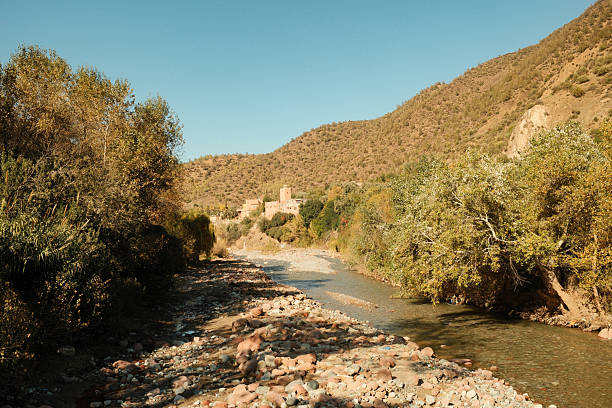 Ourika Valley river flowing through the Atlas Mountains in Morocco with traditional kasbah buildings nestled among trees