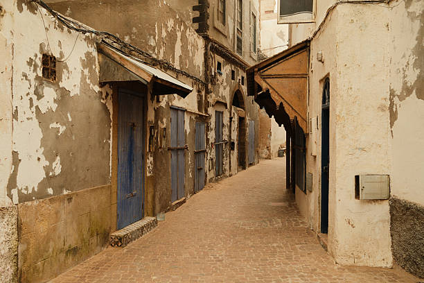 Narrow cobblestone street in the old Medina of Essaouira, Morocco, featuring weathered walls and rustic blue wooden doors