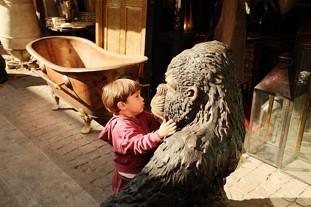 Child touching a gorilla statue, exploring an antique shop in Marrakech, Morocco, surrounded by unique items