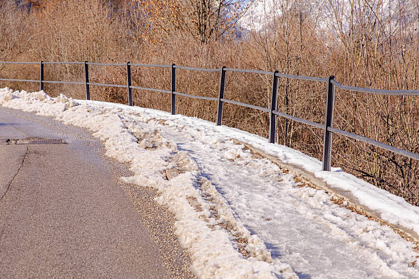 Muddy winter road with snow, railings, and bare trees