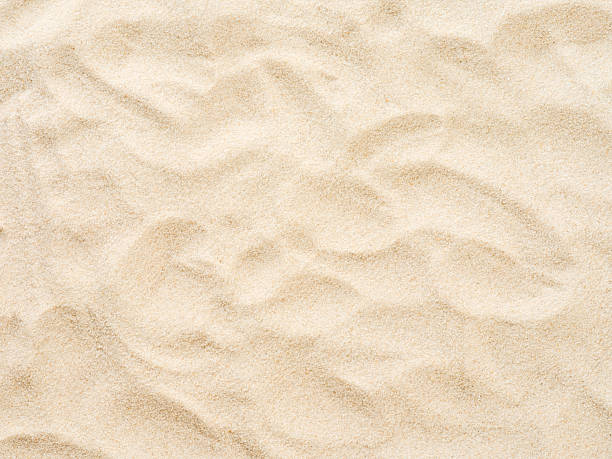 Beach sand background with natural wave pattern. Summer background of beach sand with small stones along the edges. Tourism, vacation and holidays concept. Top view.