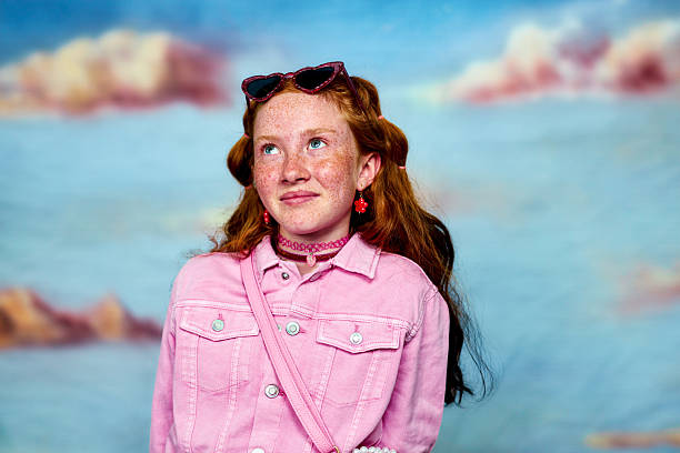 Young girl with red hair and freckles gazing thoughtfully against a cloudy background