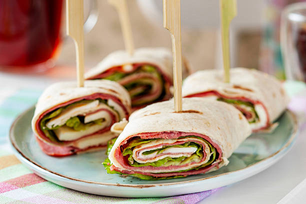 Delicious appetizer wraps with pastrami, cheese, and lettuce served on a kitchen table.