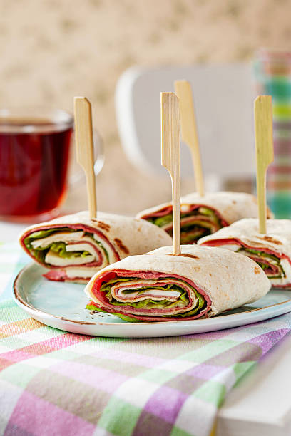 Delicious appetizer wraps with pastrami, cheese, and lettuce served on a kitchen table.