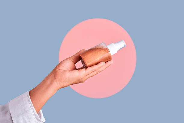 Hand holding bronzer mist spray bottle against pastel background, minimal studio shot showcasing skincare, tanning and beauty product application