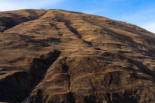 Arid mountain landscape with dry hills and eroded terrain under clear sky. Suitable for environmental and natural background use.