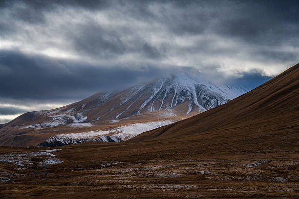 Moody alpine mountain landscape with snow-covered slopes under heavy clouds. Suitable for dramatic nature and environmental backgrounds.