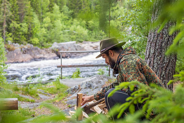 Young man chops wood for a fire, outdoor, fireplace, camfire, camp, forest, river, waterfall