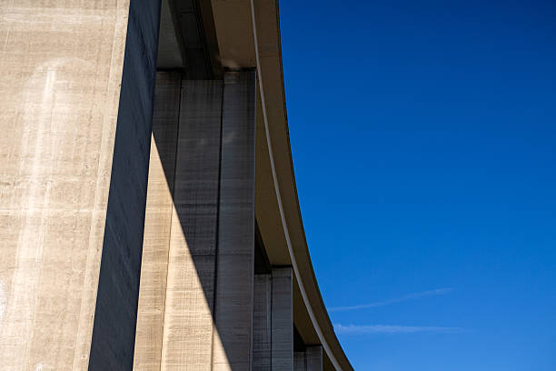 Minimalist view of a concrete bridge structure against a bright blue sky. The architectural lines and shadows highlight modern engineering design. Perfect for backgrounds, architecture concepts, and urban landscapes.
