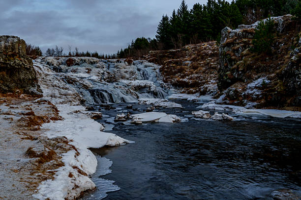 A partly frozen river pool with ice floes leads to a small winter waterfall.