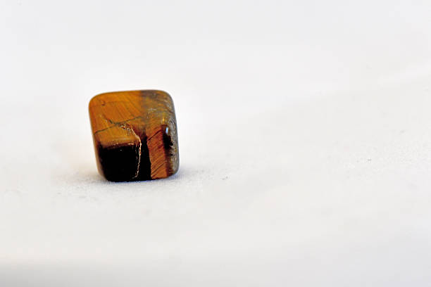 A detailed macro shot of a square-cut, polished tiger's eye mineral specimen showing characteristic golden-brown chatoyancy and silky luster, isolated on white.