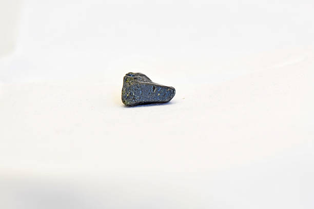 A detailed macro shot of a raw, dark grey pyrolusite mineral stone featuring a metallic luster and natural crystalline structure, isolated on a white background.