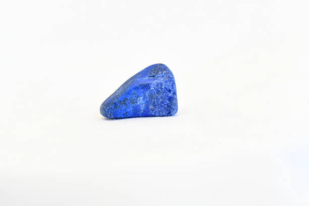 A detailed macro shot of a polished, deep blue lapis lazuli mineral specimen with natural dark inclusions, isolated on a white background.