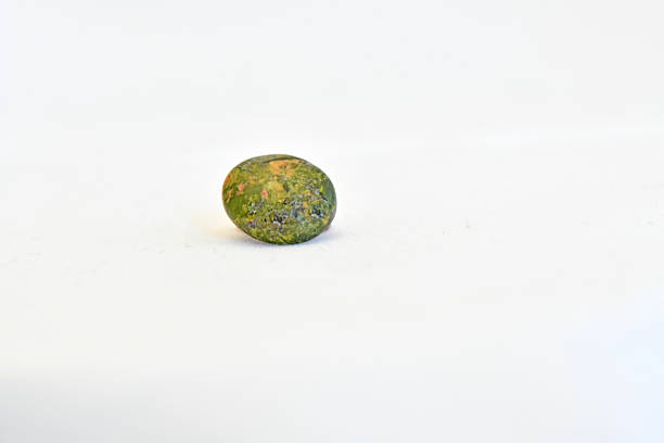 A detailed macro shot of a polished, oval unakite mineral specimen featuring its characteristic mottled green epidote and pink orthoclase feldspar patterns, isolated on a white background.