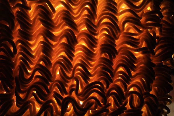 A detailed close-up of dried raw lentil rotini pasta, showcasing its spiral shape and vibrant orange hue. The tightly packed arrangement highlights the texture and structure of the pasta, emphasizing its plant-based composition. The image captures the intricate curves and edges of the pasta, revealing slight imperfections and breakages.