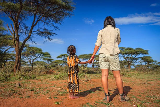 Young caucasian female volunteer holding hand of african child's hand in Ethiopian village.