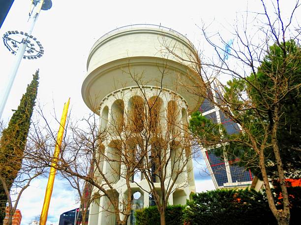 A glass cylinder structure stands right next to a traditional building, beautifully illuminated by sunlight, showcasing a fascinating contrast
