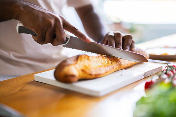 Close-up of hands slicing a crusty baguette on a white cutting board in a bright kitchen.