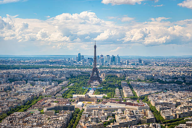 An aerial view of Paris is seen from the top of the Eiffel Tower, showing the cityscape and surrounding landmarks.