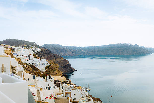 Aerial view showcasing Oia's iconic whitewashed architecture cascading down cliffs to the azure Aegean Sea. Terraced landscapes, blue-domed churches, and vibrant bougainvillea define this charming Cycladic village in Santorini, Greece.