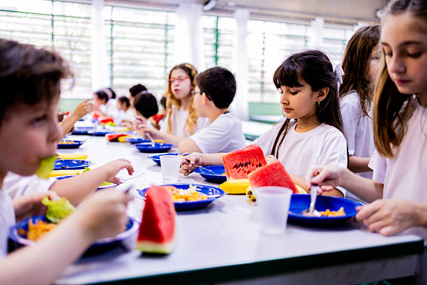 Schoolgirl having lunch with classmates in the cafeteria at school