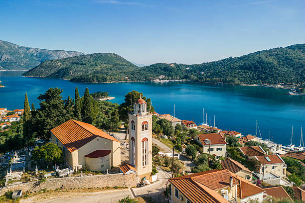 Aerial view of small town with a beautiful bay, Vathi, Ithaca, Greece. There is a church with bell tower and traditional Mediterranean houses near waterfront. It's a beautiful sunny summer morning. There is a small island in the middle of the bay.