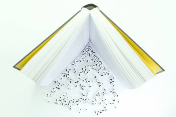 A book is open and lying flat with pages visible. Letters are scattered around the book on the white surface, suggesting a playful or creative activity with words and letters.