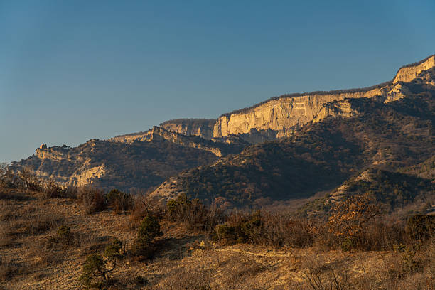 Arid mountain ridge with layered rock formations and dry vegetation under clear sky. Suitable for environment, geology, and natural background use.