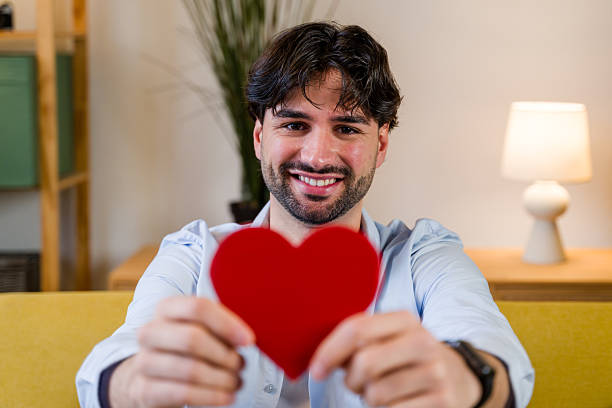 Smiling man offering a red heart, symbolizing love, care, and gratitude